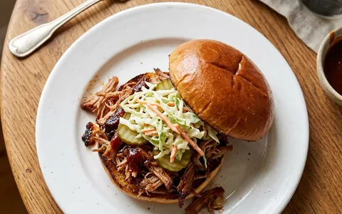 A white plate of barbecue pulled pork on a bun, photographed from above.
