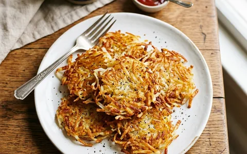 A white plate of crispy golden hash browns, photographed from above.