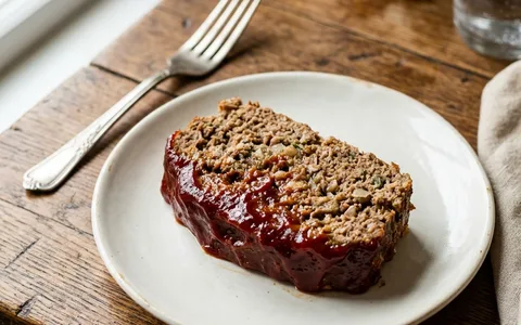 A slice of meatloaf with tomato glaze on a white plate, photographed from above.
